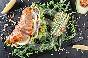 Sandwich with tuna, avocado, fresh arugula and greens on black shale board over black stone background. Healthy food concept