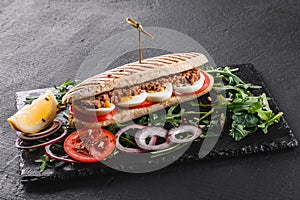 Sandwich with tuna, eggs, fresh vegetables and greens on black shale board over black stone background. Healthy food concept