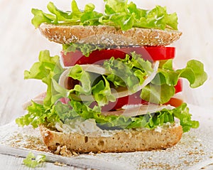 Sandwich with turkey and fresh vegetables on a wooden background