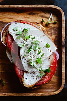 Sandwich with turkey meat and fresh vegetables served with microgreens on a wooden plate