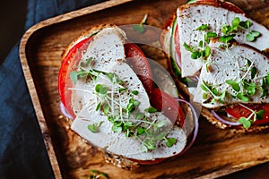 Sandwich with turkey meat and fresh vegetables served with microgreens on a wooden plate