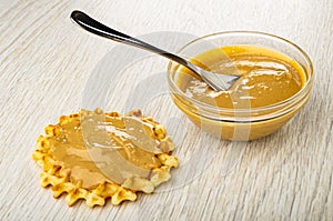 Sandwich from waffle with peanut butter, spoon in bowl with peanut paste on table