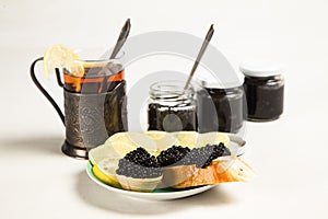 Sandwiches with black sturgeon caviar, lemon slice and tartlet with black caviar on a plate.