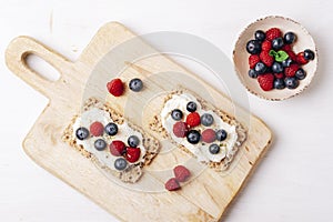 Sandwiches with blueberries and raspberries on cutting board on white wooden table. Healthy breakfast. Top view, flat