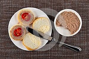 Sandwiches from bread, liver pate and tomato in plate, knife, bowl with liver pate on mat. Top view