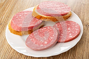 Sandwiches from bread with sausage, slices of sausage in plate on wooden table