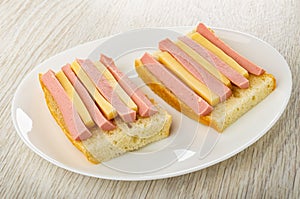 Sandwiches from bread  with sausages and cheese in white plate on wooden table