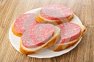 Sandwiches from bread with smoked sausage in plate on wooden table