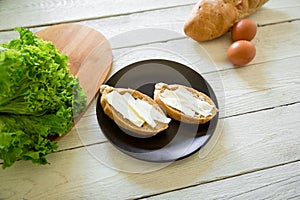 Sandwiches with butter on black plate and eggs, bread on wooden table. Delicious natural breakfast