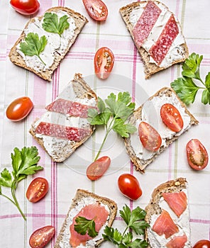 Sandwiches with cherry tomatoes, parsley, salmon and salami wooden rustic background top view