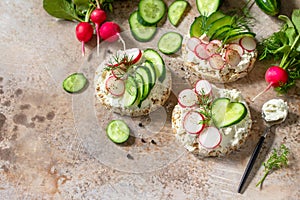 Sandwiches crispbread with ricotta, radish and fresh cucumber on a light or slate countertop.