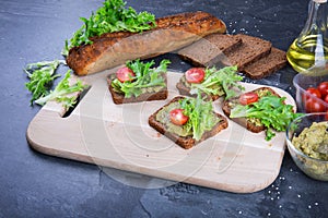 Sandwiches on a cutting desk. Crunchy cut bread, salad leaves, red tomatoes, oils and guacamole sauce on a gray table