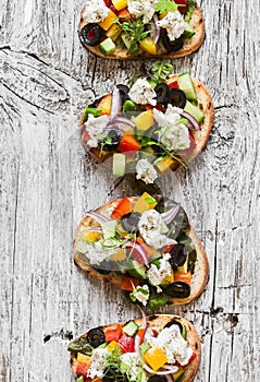 Sandwiches with feta, tomatoes, cucumbers and olives. Greek salad bruschetta style on a rustic board. Delicious appetizer