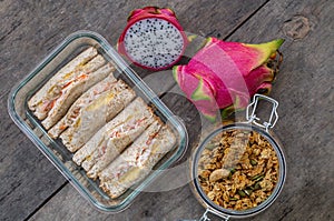 sandwiches in glass box with granola and pitaya fruit on wooden table for breakfast, top view