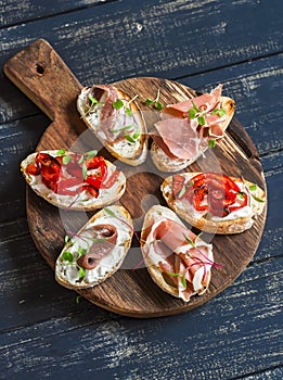 Sandwiches with goat cheese, anchovies, roasted peppers, ham on a wooden rustic board.