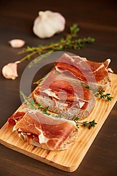 Sandwiches made from hand-made rye bread and thin chopped fresh bacon. Fresh green thyme on a wooden board. Succulend bacon on a w