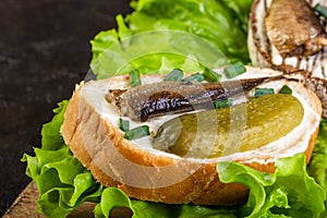 Sandwiches made of sprots and cucumbers on lettuce leaves and wood board