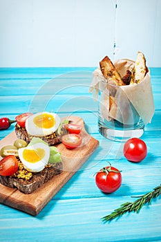 Sandwiches with olive, quail eggs, cherry tomatoes and potatoes on a wooden blueboard.