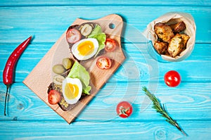 Sandwiches with olive, quail eggs, cherry tomatoes and potatoes on a wooden blueboard