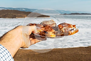 Sandwiches with omul on a white round plate. A plate of sandwiches in hands. Winter Baikal in ice.
