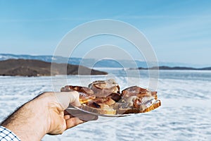 Sandwiches with omul on a white round plate. A plate of sandwiches in hands. Winter Baikal in ice. Fish dishes.