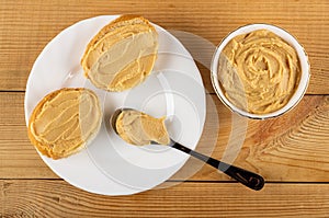 Sandwiches with peanut paste, spoon in plate, peanut butter in bowl on table. Top view