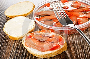 Sandwiches with pink salmon and butter, fork on jar with salmon on wooden table