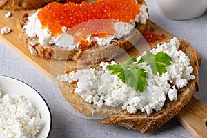 Sandwiches with red caviar on a rye bread and cottage cheese. Wooden cutting Board. Close up