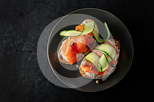 Sandwiches with smoked trout, cream cheese, fresh cucumber, and capers on a black plate