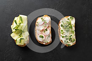 Sandwiches with sundries tomatoes, fresh radish, microgreens, cream cheese on black . Top view photo