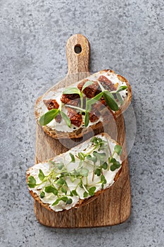 Sandwiches on toast with sun-dried tomatoes, fresh radish microgreens, cream cheese on grey . Top view. Vertical format photo