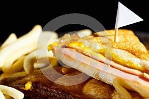 Sandwish ham cheese with frenchfries on wood plate and black bac photo