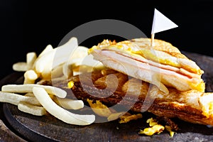 Sandwish ham cheese with frenchfries on wood plate and black background