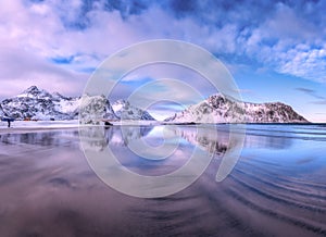 Sandy beach with blue sea reflected in water and rocks in snow