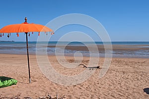 Sandy beach, blue sky and orange umbrella at east point reserve