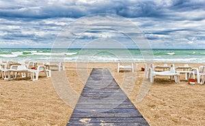 Sandy beach on cloudy day with wooden pathway and empty sun beds