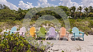 Sandy beach with colorful beach sunbeds, surrounded by green trees, on a sunny day