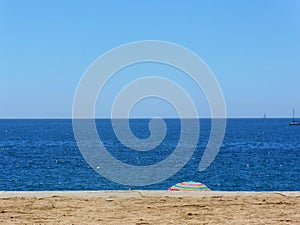 Sandy beach with crystal blue sea with lone umbrella in distance