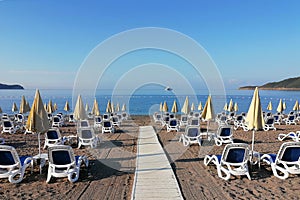 Sandy beach with deck chairs and umbrellas. In the background blue sea, sky and the yacht