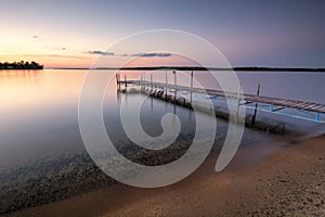 Sandy beach and dock beside lake at sunset. Minnesota, USA