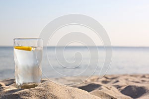Sandy beach with glass of refreshing lemon drink on hot summer day