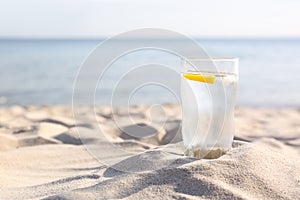 Sandy beach with glass of refreshing lemon drink on hot summer day