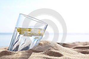 Sandy beach with glass of refreshing lemon drink on summer day, space for text