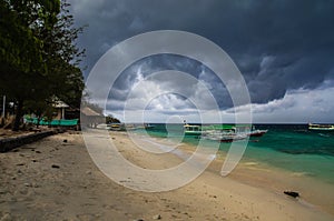 Sandy beach with moored Indonesian boats on the tropical island of Gili Meno. Heavy leaden clouds hung over the beach, a