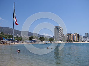 Sandy beach panorama at bay of ACAPULCO city in Mexico with luxury hotels buildings and mexican flag