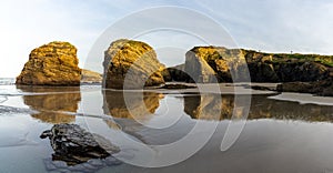 Sandy beach panorama with tidal pools and jagged broken cliffs behind in warm evening light