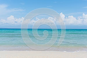 Sandy beach with rolling calm wave of ocean on sunny day on background white clouds in blue sky