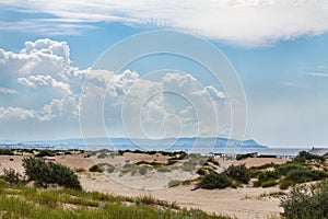 Sandy beach with sand dunes by the sea against the blue sky.