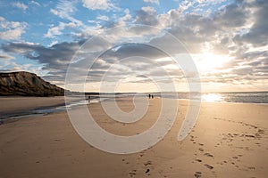 Sandy beach at the sea under a sky painted with clouds and a golden sun, showing an Amazing colorful sunset. Picturesque