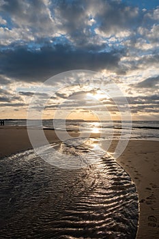 Sandy beach at the sea under a sky painted with clouds and a golden sun, showing an Amazing colorful sunset. Picturesque